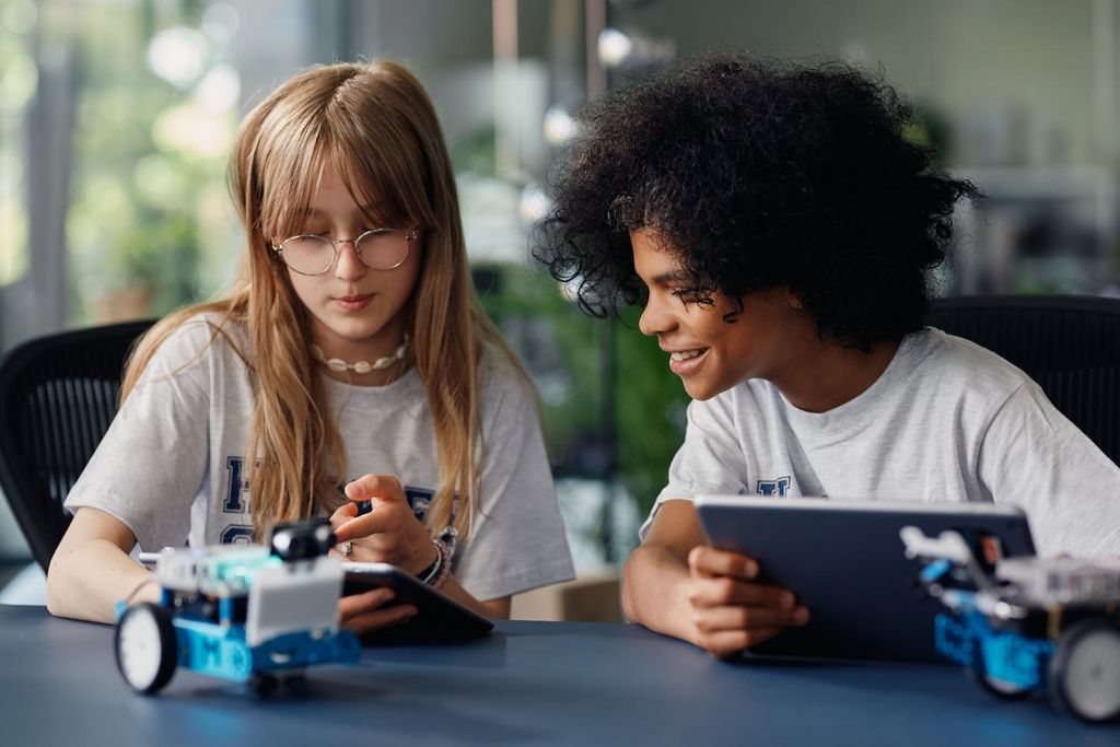 Zwei Kinder aus der Hacker School programmieren zwei kleine Roboter.